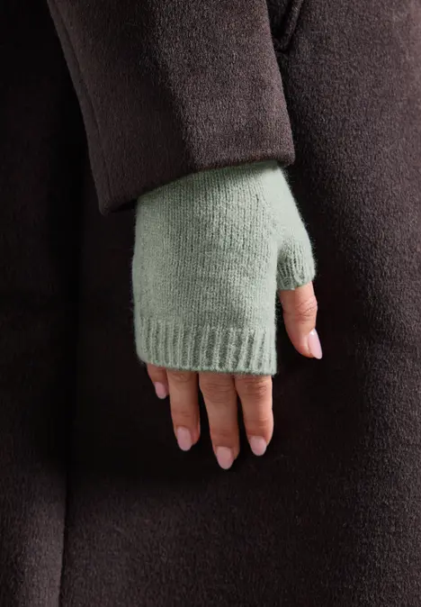 Nahaufnahme einer Hand in hellgrünem Fingerhandschuh und dunkelbraunem Mantel.