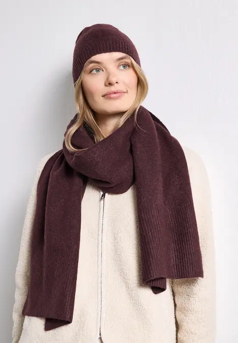 Femme en veste polaire beige, écharpe et bonnet bordeaux