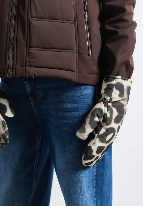 Persoon draagt een bruine jas, een blauwe spijkerbroek en witte wanten met zwarte vlekken.