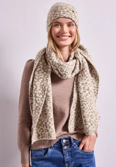 Jonge vrouw lacht, draagt beige gebreide muts en sjaal, bruine trui.