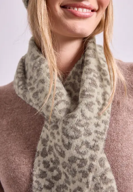 Een lachende vrouw draagt een pluche sjaal met luipaardmotief bij een bruine trui.
