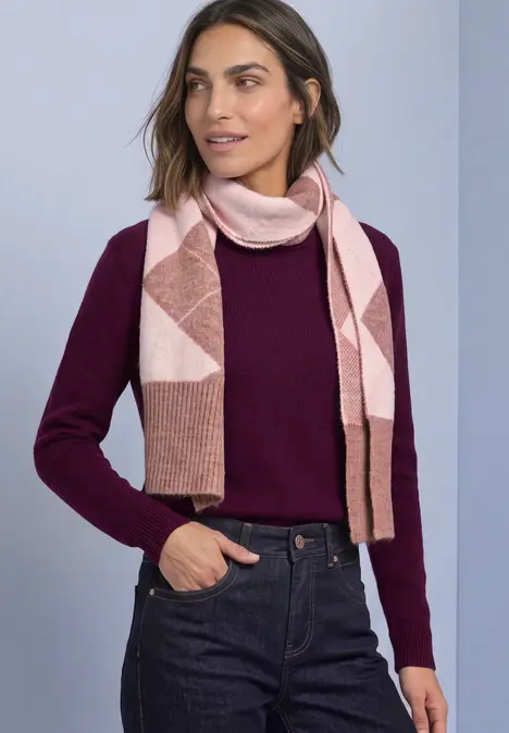Frau in bordeauxrotem Pullover, Jeans und rosa Schal mit geometrischem Muster.