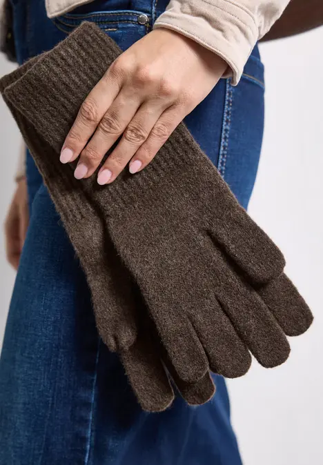 Braune, gestrickte Fünffinger-Handschuhe, in einer Hand gehalten, vor einer Jeanshose.
