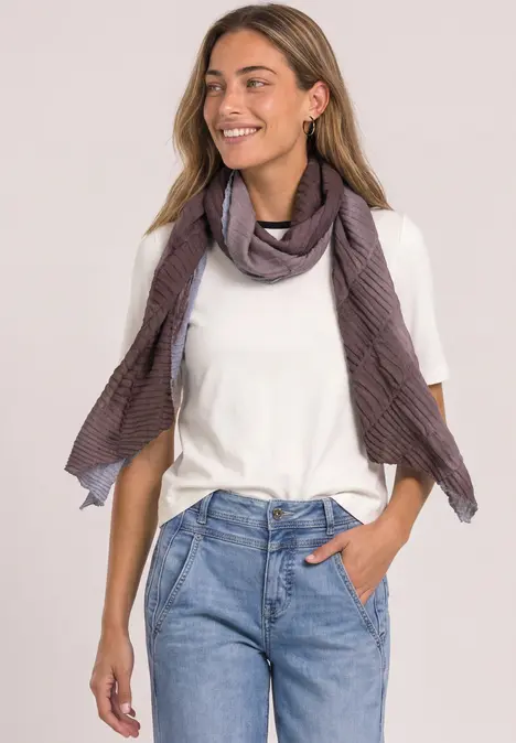 Frau lächelt in weißem T-Shirt, blauen Jeans und lila gestreiftem Schal.