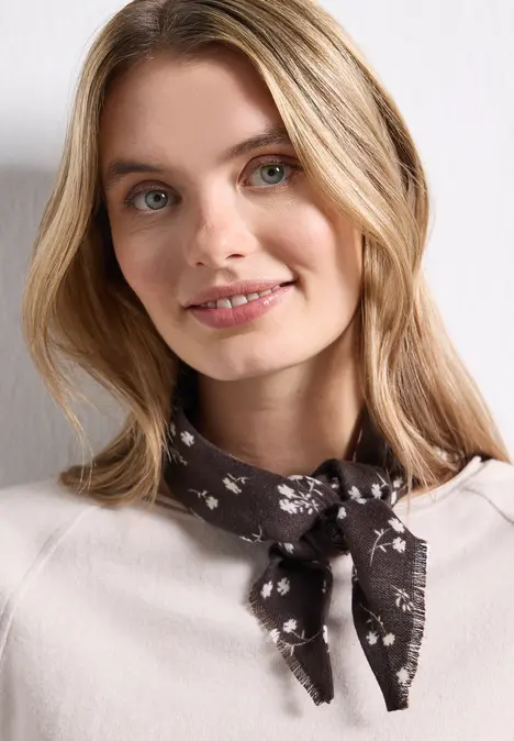 Junge Frau mit blondem Haar trägt helles Oberteil und geblümtes Halstuch, sie lächelt leicht ins Bild.