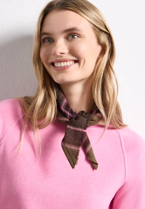 Eine lächelnde Frau mit langen blonden Haaren trägt einen pinken Pullover und ein braunes, gemustertes Halstuch.