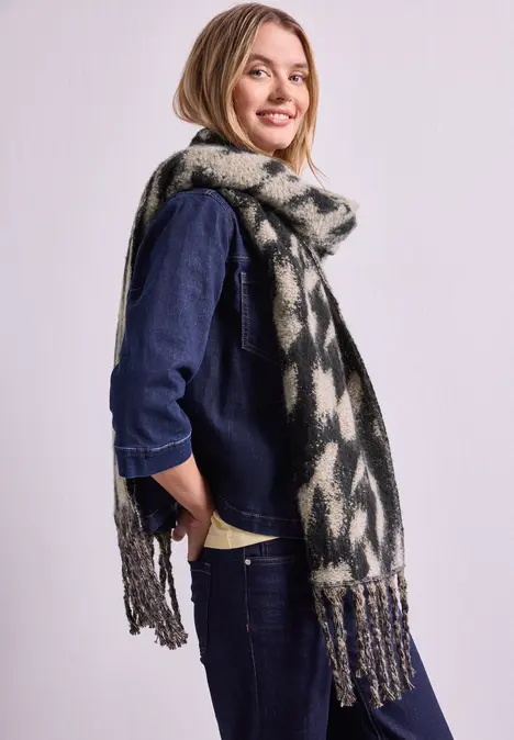 Glimlachende vrouw in denim met een lange, geprinte sjaal voor een lichte achtergrond.