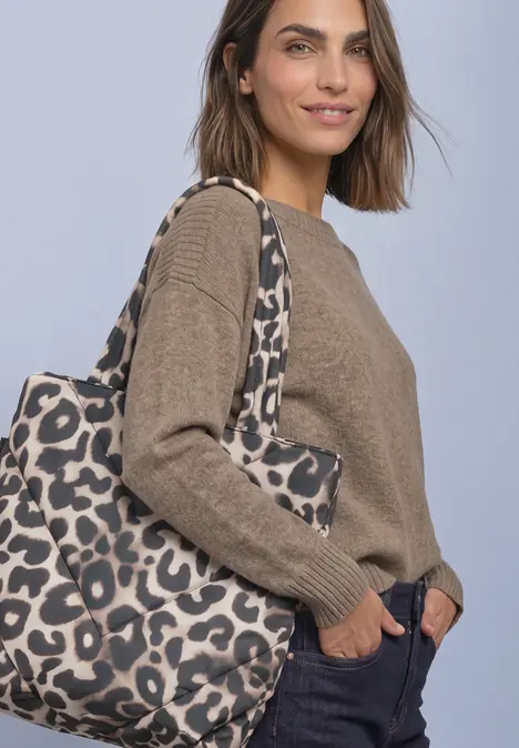 Eine Frau trägt einen braunen Pullover, eine dunkelblaue Hose und eine große Leoparden-Print-Tasche.