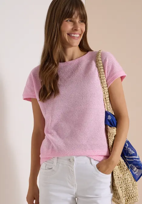 Frau im rosa T-Shirt und weißen Jeans trägt handgewebte Schultertasche mit blauem Tuch.