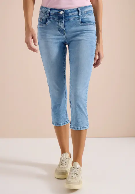 Frau trägt hellblaue Capri-Jeans und weiße Sneaker.