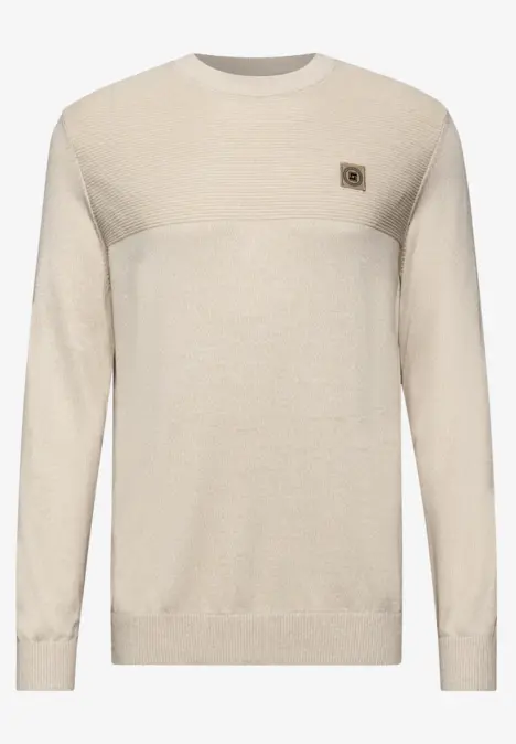 Pull beige à col rond avec un petit emblème sur la poitrine.