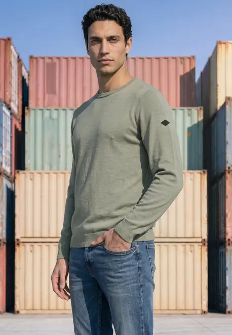 Un homme en pull vert et jean se tient devant des conteneurs colorés.