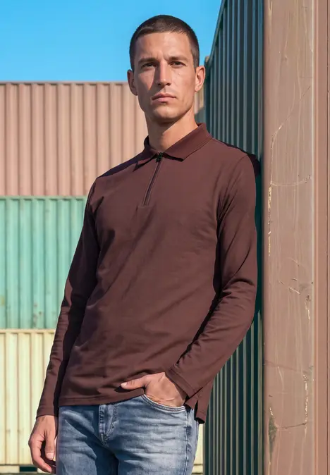 Un homme en polo marron et jean s'appuie devant des conteneurs colorés sous un ciel bleu.