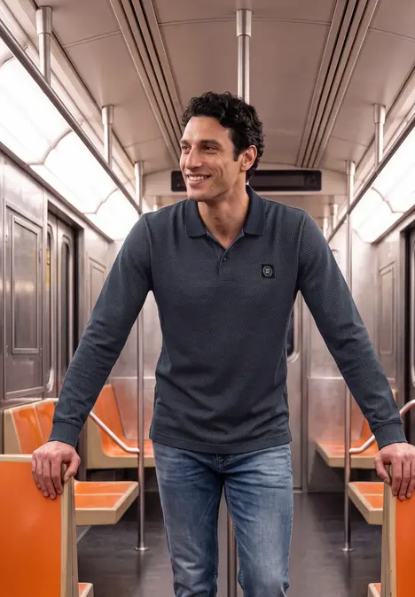 Ein lächelnder Mann in Jeans und Polo steht in einer U-Bahn mit orangefarbenen Sitzen.