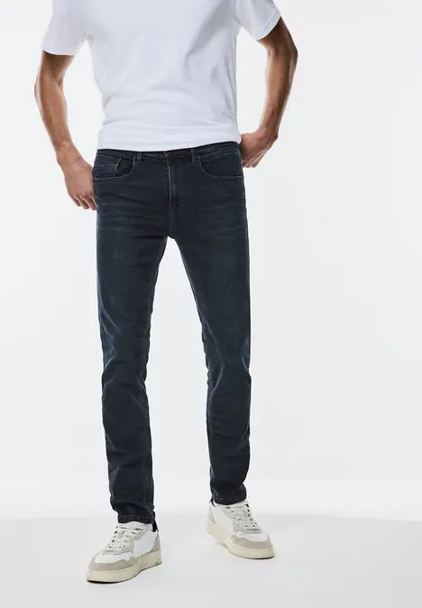 Man met wit T-shirt, donkere spijkerbroek en witte sneakers.