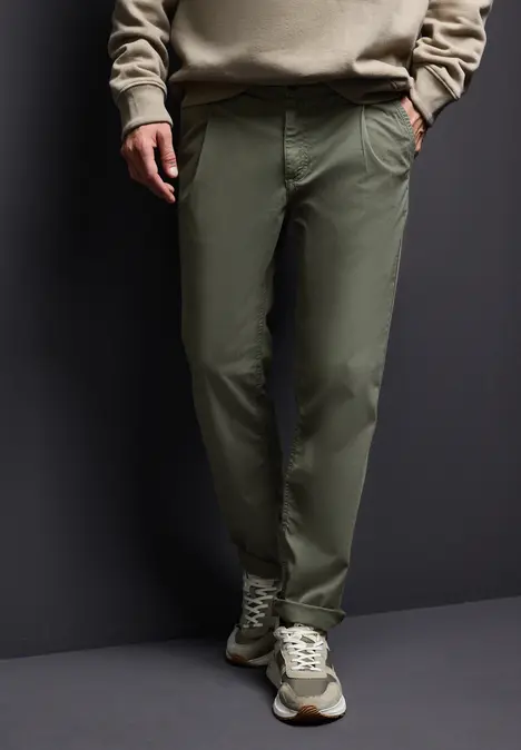 Homme portant un pantalon vert, un pull beige et des baskets.