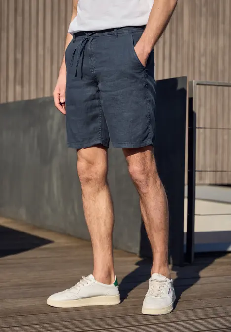 Homme sur terrasse en bois, en baskets blanches, short bleu marine et T-shirt blanc.