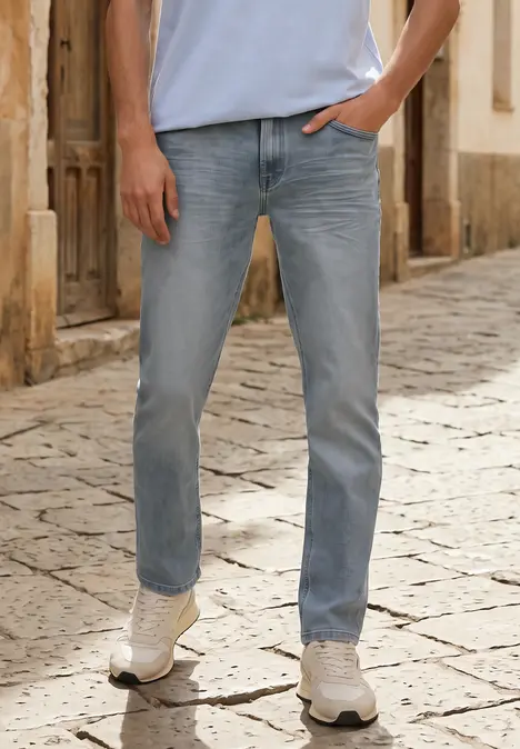 Persoon draagt lichtblauwe jeans en witte sneakers, staat met hand in zak op kinderkopjes.