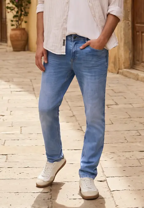 Een man draagt lichtblauwe jeans en witte sneakers op een geplaveid pad.