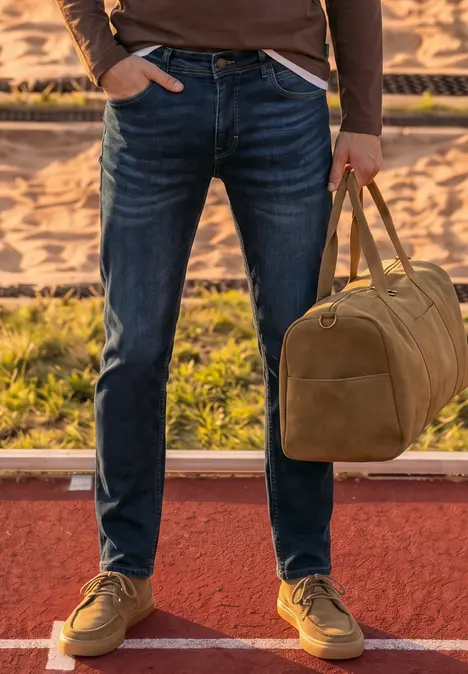 Person mit blauen Jeans, braunen Schuhen und brauner Tasche steht auf roter Laufbahn.
