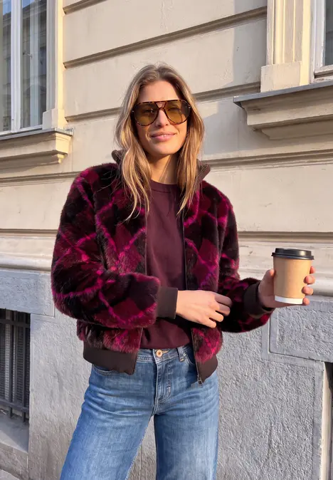 Femme en veste tendance tenant un gobelet de café à emporter devant un mur citadin