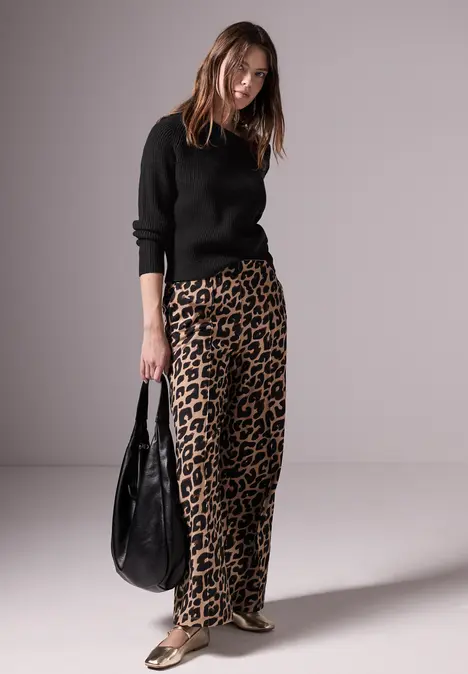 Frau mit schwarzem Pullover, Leo-Hose, goldenen Schuhen und schwarzer Tasche.