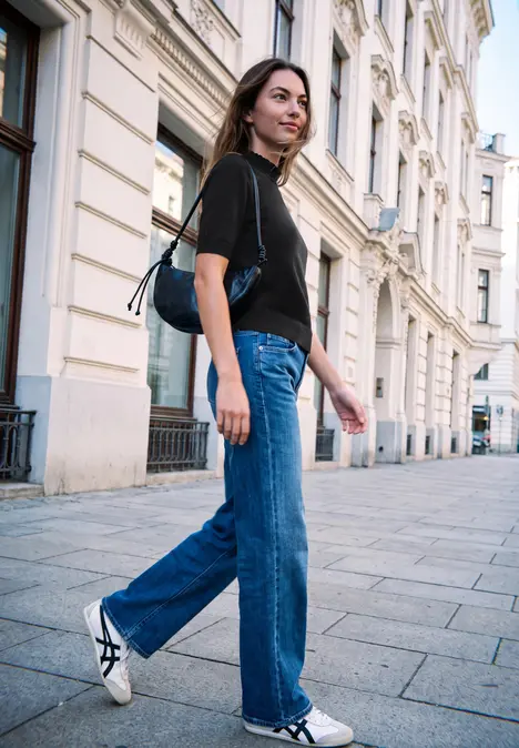 Frau in schwarzem Shirt und blauer Jeans spaziert an historischen Stadthäusern vorbei.