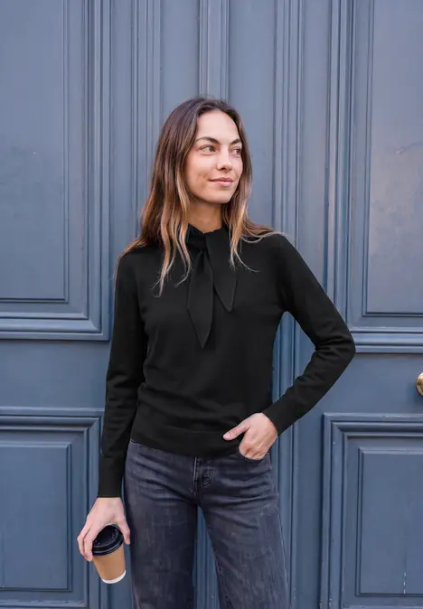 Jonge vrouw in casual outfit met koffiebeker voor een blauwe deur.