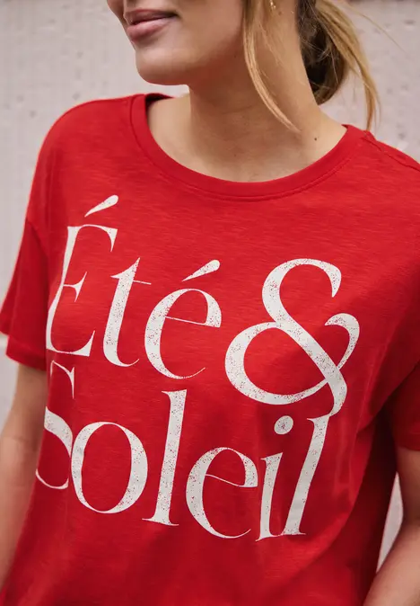 Frau trägt rotes T-Shirt mit weißem Schriftzug 'Été & Soleil'