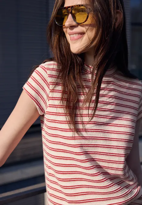Frau in rot-weiß gestreiftem T-Shirt lehnt lässig am Geländer im Freien.
