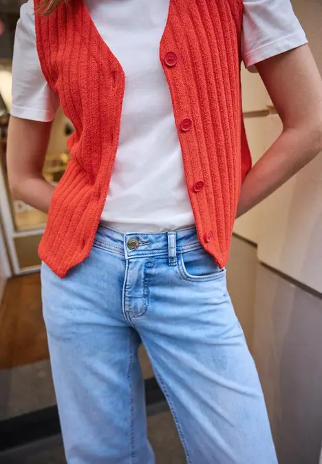 Person trägt weißes T-Shirt, hellblaue Jeans und rote, gestrickte Weste