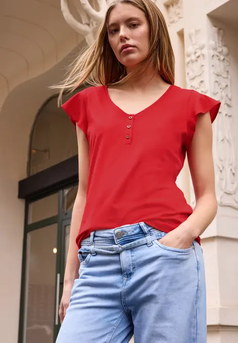 Vrouw in rood shirt en blauwe jeans voor versierde gebouwentree.
