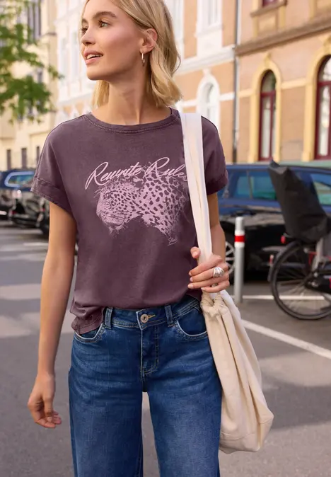 Junge Frau spaziert in Jeans und T-Shirt mit Tasche auf städtischer Straße