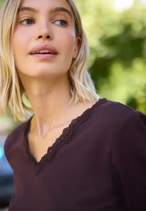 Blonde Frau trägt dunkelviolettes Spitzen-Shirt und blickt nach oben im Freien.