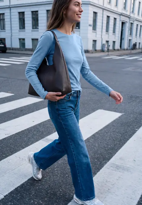 eine Frau geht mit grauer Tasche und blauer Jeans über einen Zebrastreifen