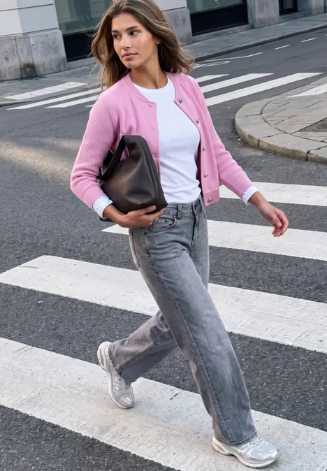 Frau überquert Zebrastreifen mit rosa Cardigan, weißem Shirt, grauen Jeans und silbernen Sneakers.