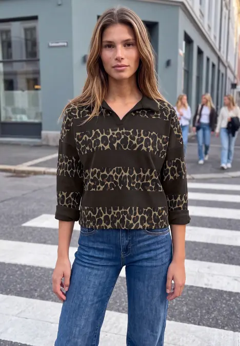 Frau in leo-gemustertem Pullover und Jeans auf einem städtischen Zebrastreifen.