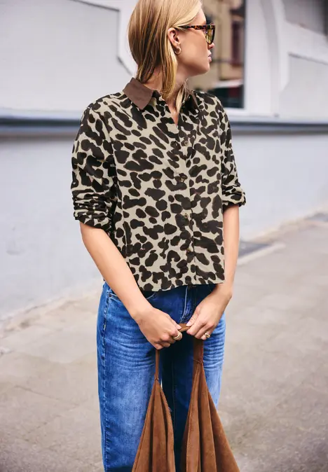 Frau mit Leopardenbluse, blauen Jeans und großer brauner Tasche spaziert die Straße entlang.