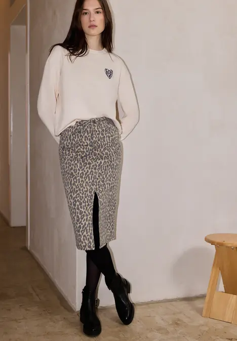Vrouw in beige trui en midi rokje met luipaardprint en split, zwarte panty en plateau loafers.