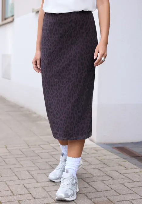 Eine Person trägt einen midi-Rock mit dezentem Leopardenmuster, weiße Socken und chunky Sneaker auf Pflaster.
