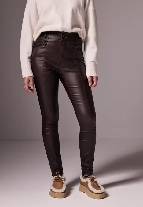 Frau trägt braune Lederhose, weißen Pullover und braune Schuhe.