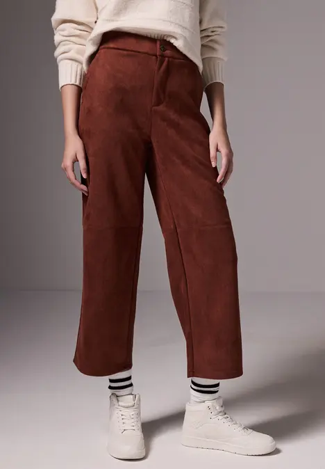 Frau mit brauner Hose, cremefarbenem Pullover und weißen Sneakern.