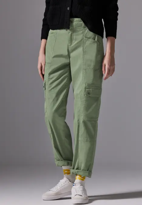 Frau trägt grüne Cargohose, schwarze Jacke und weiße Sneaker.