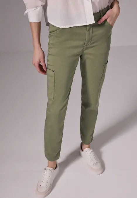 Person trägt grüne Cargohose, weißes Hemd und weiße Sneaker.