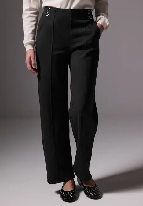 Frau mit schwarzer Hose, weißem Pullover und schwarzen Schuhen mit Nieten.