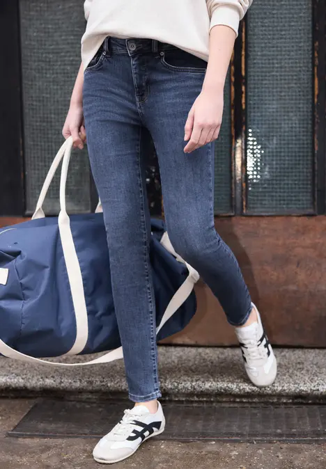 Persoon loopt op straat met een donkerblauwe spijkerbroek, witte sneakers en een blauwe reistas.