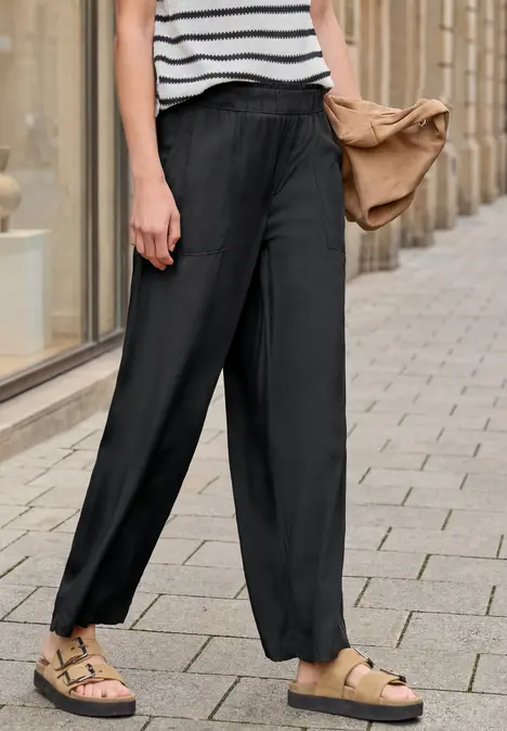Eine Person trägt eine lässige schwarze Hose mit Bündchen, gestreiftes Top und Sandalen.
