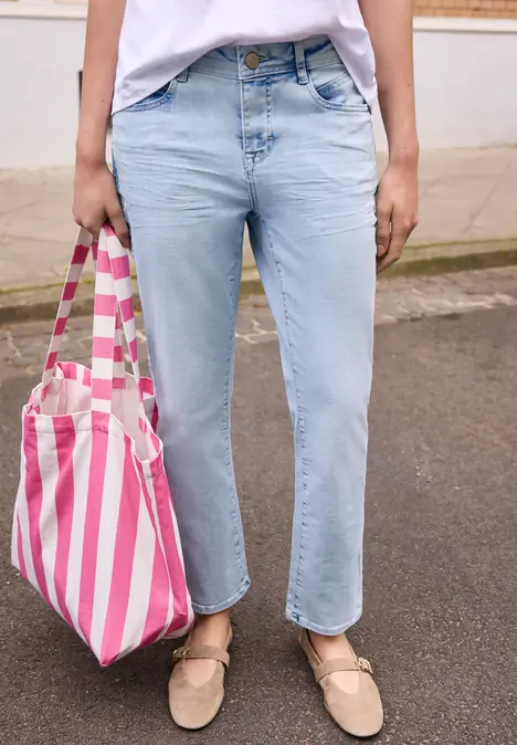 Persoon draagt lichtblauwe spijkerbroek, beige loafers en heeft een roze-wit gestreepte tas.