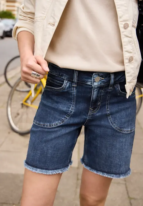Persoon in donkerblauwe jeansshorts en licht shirt, staande bij een fiets.