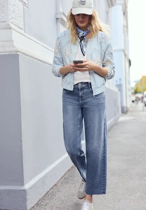 Persoon in casual jeans, licht overhemd en sneakers, gebruikend mobiel voor een wit huis.